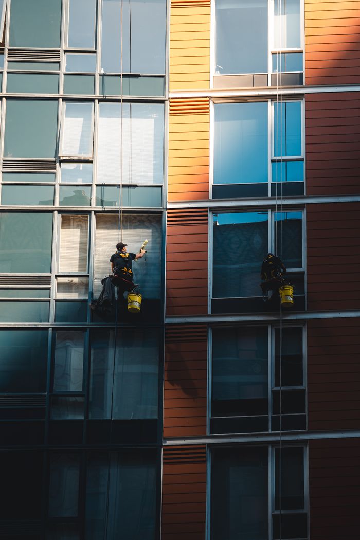 journey Two workers hanging to clean windows on a modern skyscraper facade.