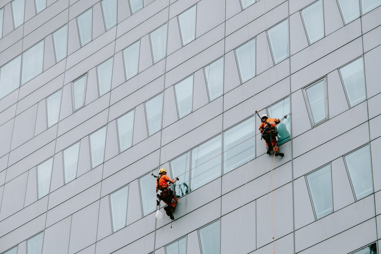 services-04 High-rise window washers in safety gear cleaning a skyscraper facade.